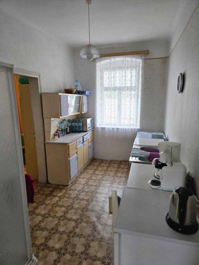 Einfache Küche mit älteren Einbauschränken, Fenster und gemustertem Fliesenboden.