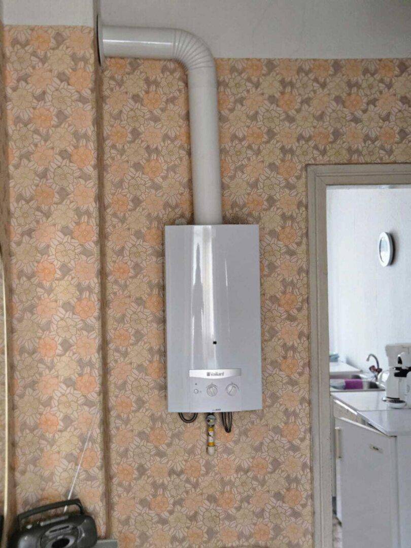 Detailansicht eines an der Wand montierten Warmwasserbereiters im Flur mit floraler Tapete.