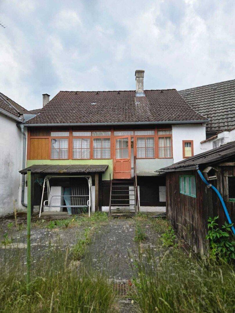 Rückansicht eines Einfamilienhauses mit verglastem Anbau und verwildertem Garten.