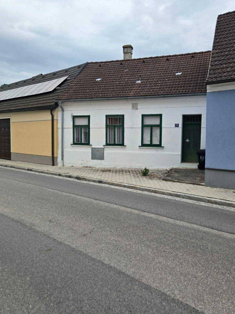 Vorderansicht eines Einfamilienhauses von der Straße mit grünen Fensterläden.