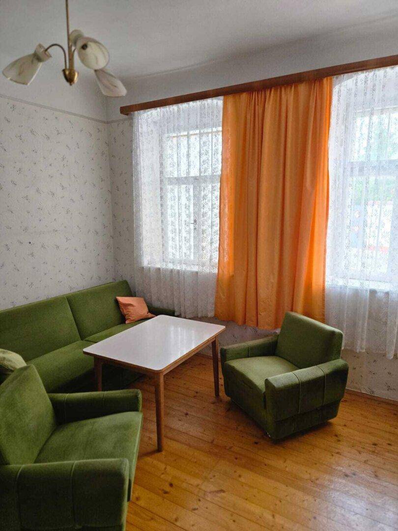 Helles Wohnzimmer mit grüner Sitzgruppe, Holzboden und großen Fenstern.