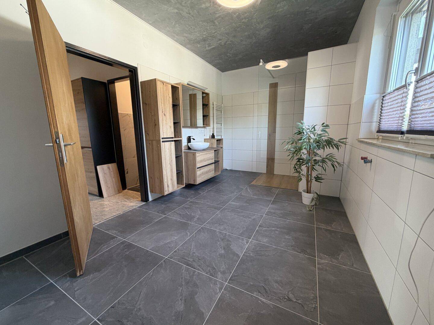 Modernes Badezimmer mit Holzmöbeln, begehbarer Dusche und großem Fenster.
