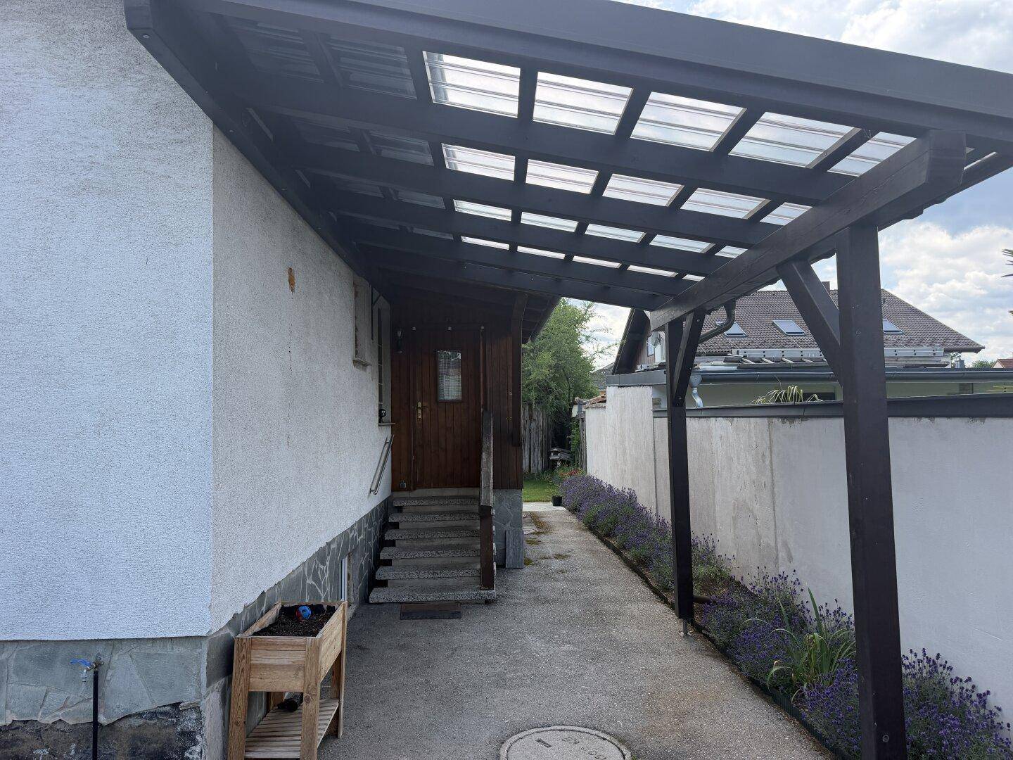 Eingangsbereich des Hauses mit überdachtem Carport und Blumenbeet.