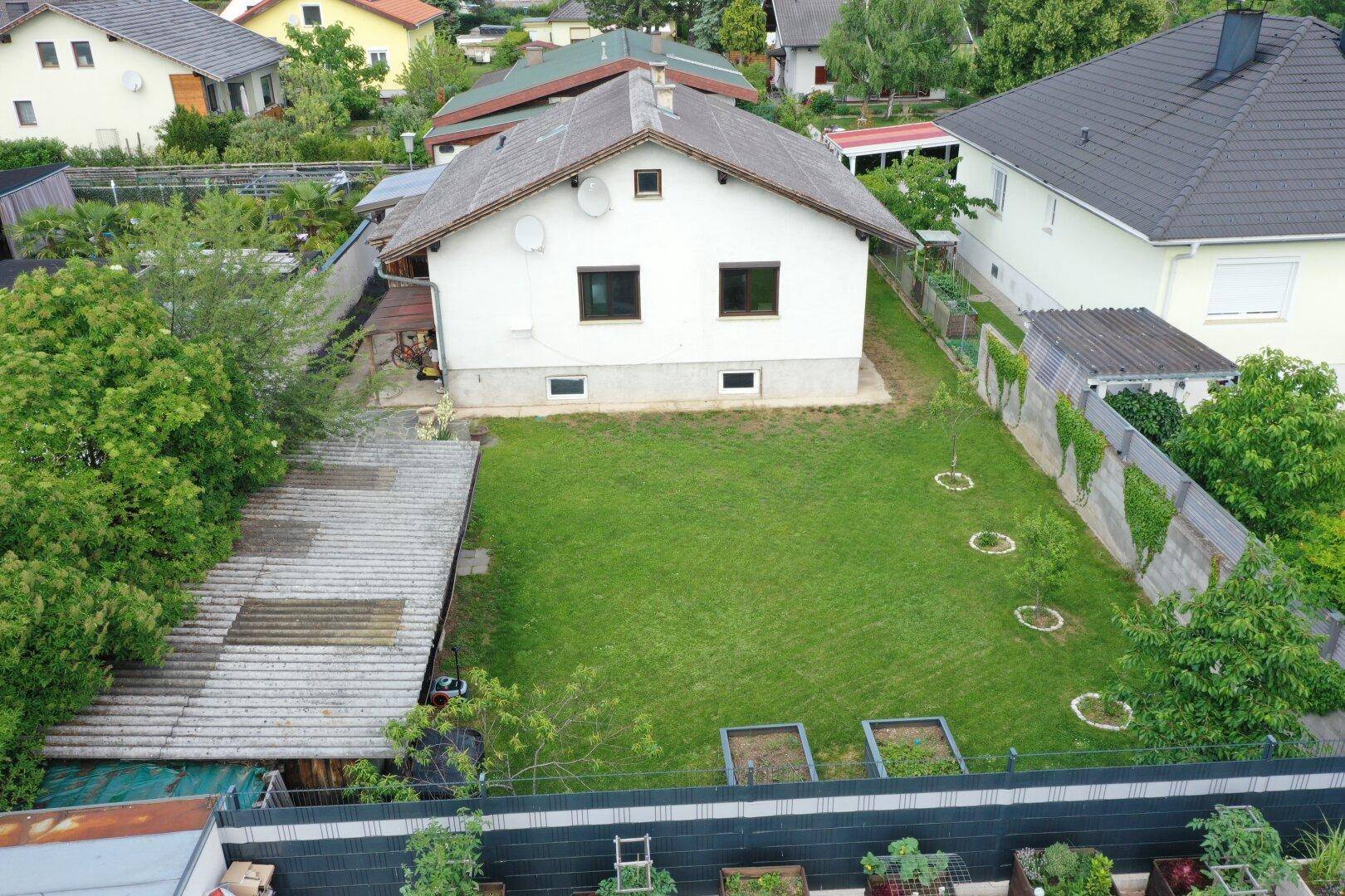 Luftaufnahme eines Einfamilienhauses mit großem Rasen, Hochbeeten und umliegenden Gärten.