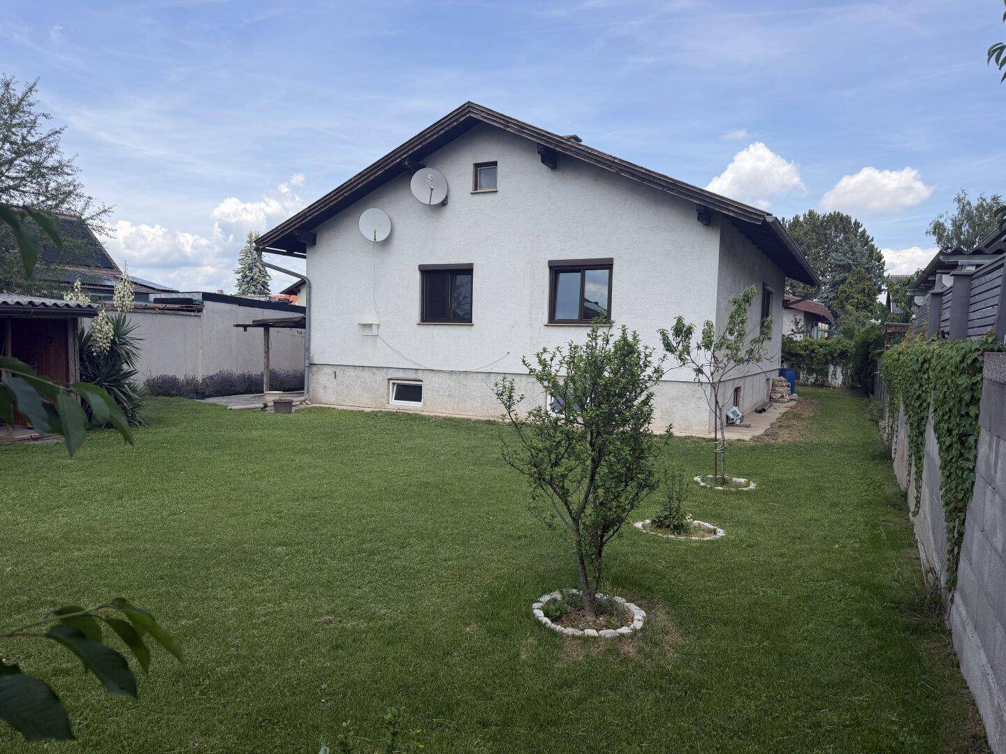 Seitenansicht des Hauses vom Garten aus mit weißer Fassade und grüner Rasenfläche.