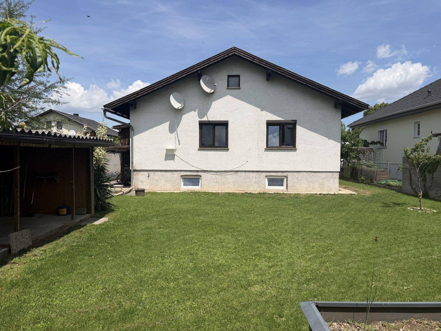 Rückansicht des Einfamilienhauses mit weißer Fassade, Fenstern und gepflegtem Rasen.