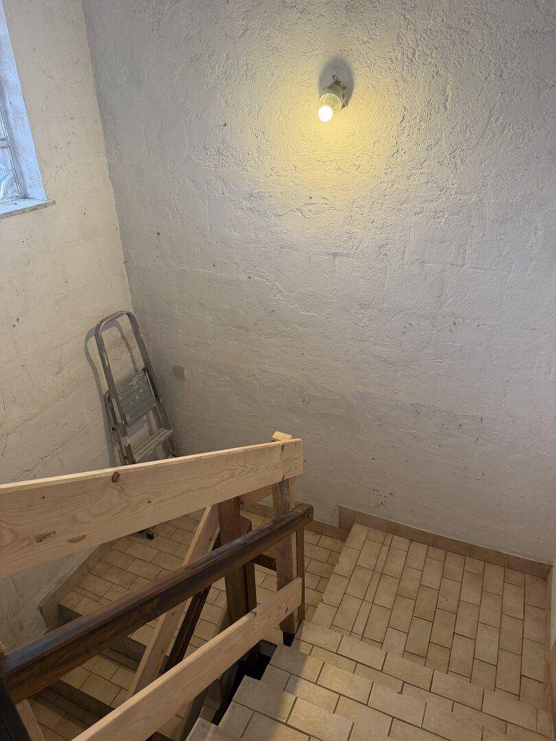 Treppenabgang zum Keller mit gefliesten Stufen und rauer Wandstruktur.