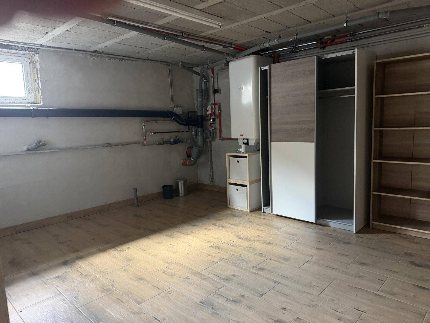 Heizungsraum im Keller mit Boiler, Rohren und Schränken.