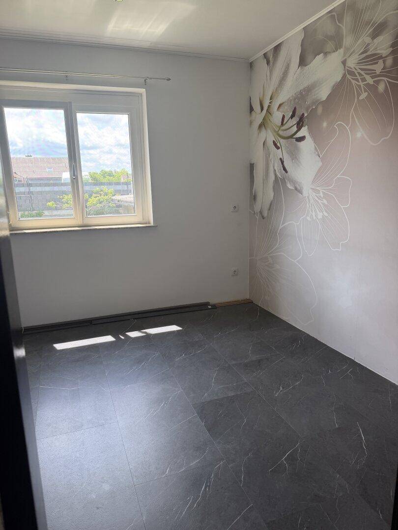 Schlafzimmer mit floraler Tapete, dunklem Fliesenboden und großem Fenster.