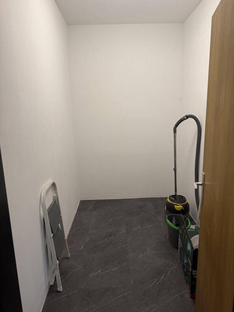 Praktischer Abstellraum mit dunklem Fliesenboden und Leiter.