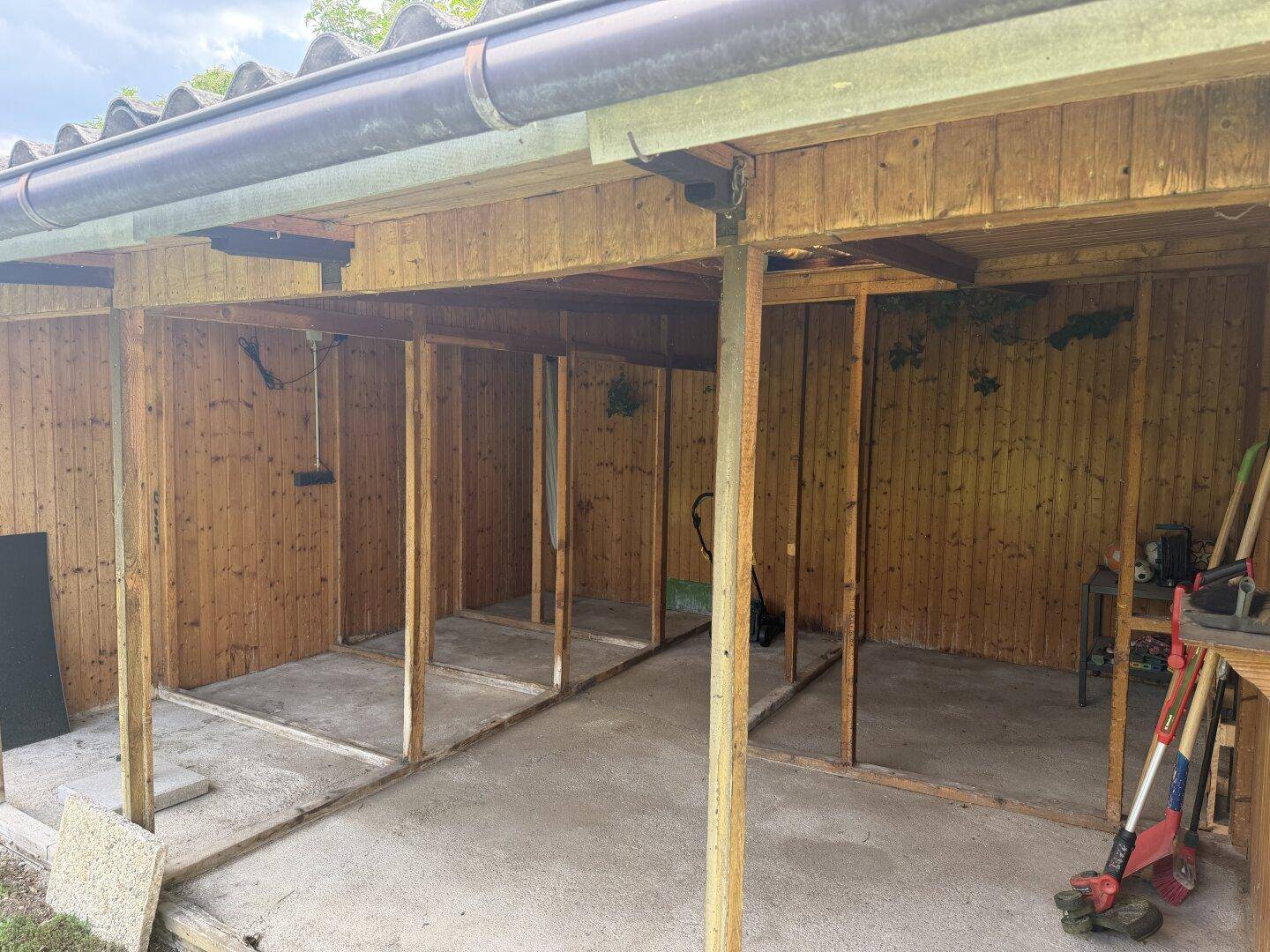 Offener Holzunterstand mit Holzverkleidung und Betonboden, nutzbar als Carport oder Lagerfläche.