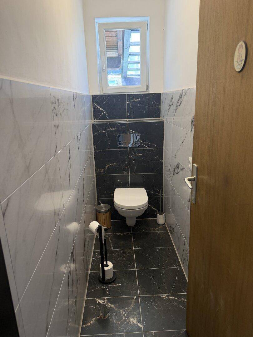 Modernes Gäste-WC mit dunklen Marmorfliesen und wandhängendem WC.