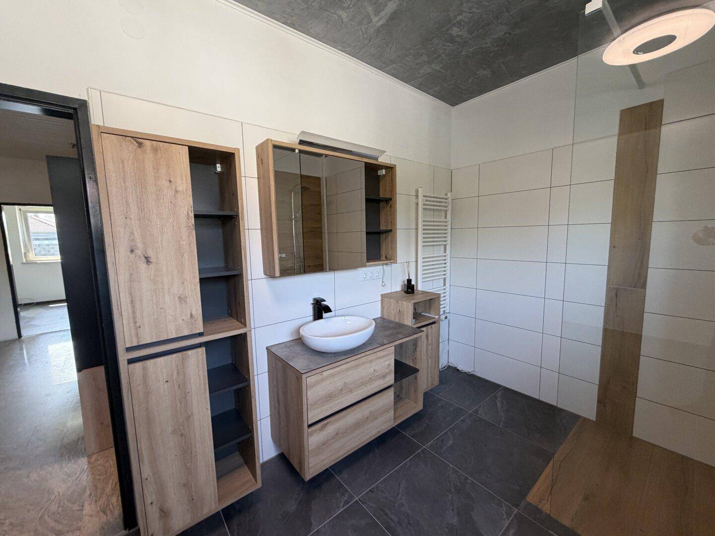 Badezimmer mit modernem Waschtisch, Spiegelschrank und Holzschränken.