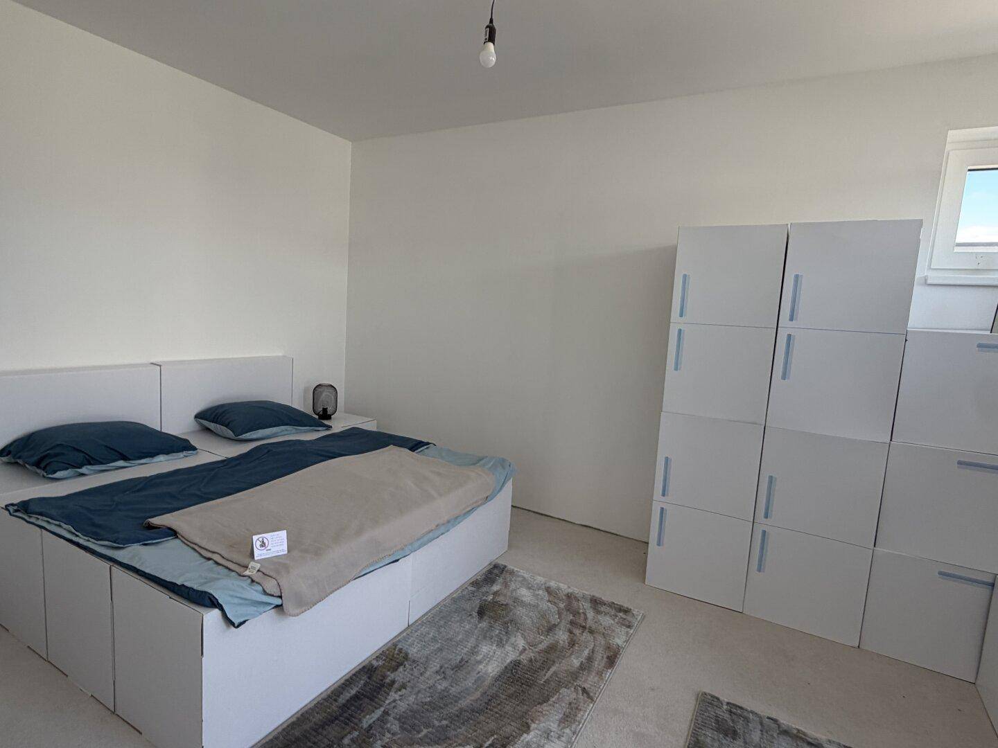 Helles Schlafzimmer mit modernem Bett und weißen modularen Schränken, gut beleuchtet und geräumig.