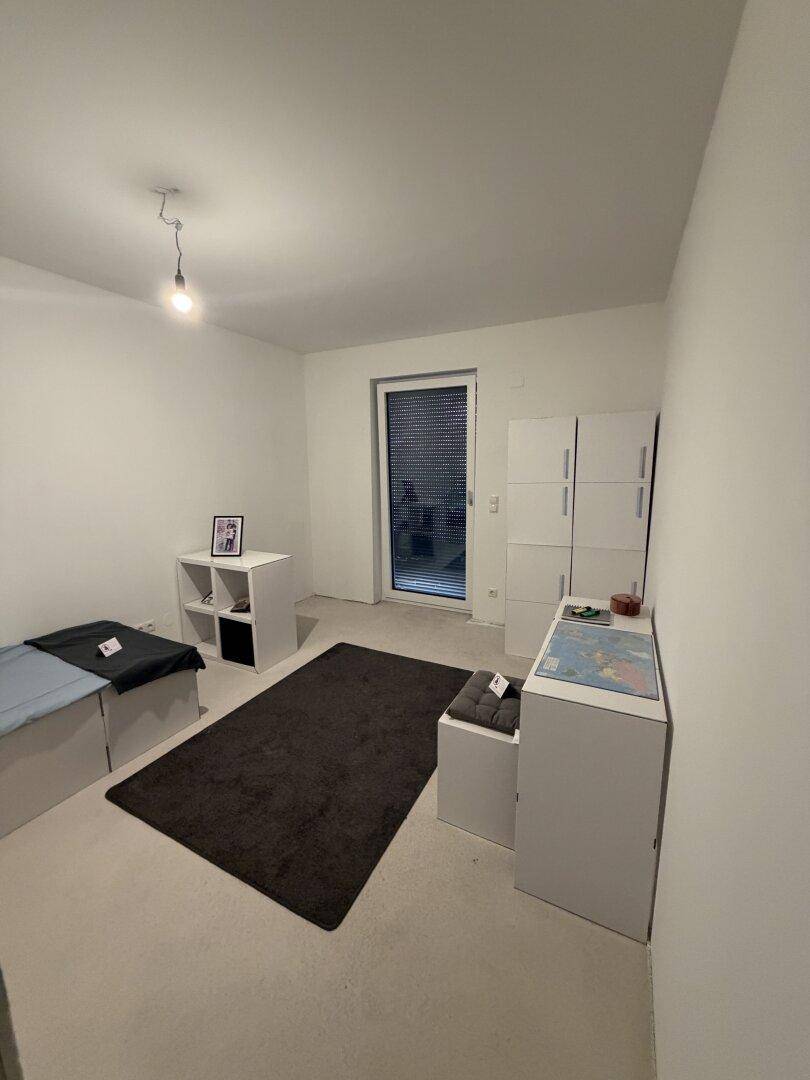 Helles Schlafzimmer mit Einzelbett und Fenster mit Rollladen, funktional eingerichtet und gut belichtet.