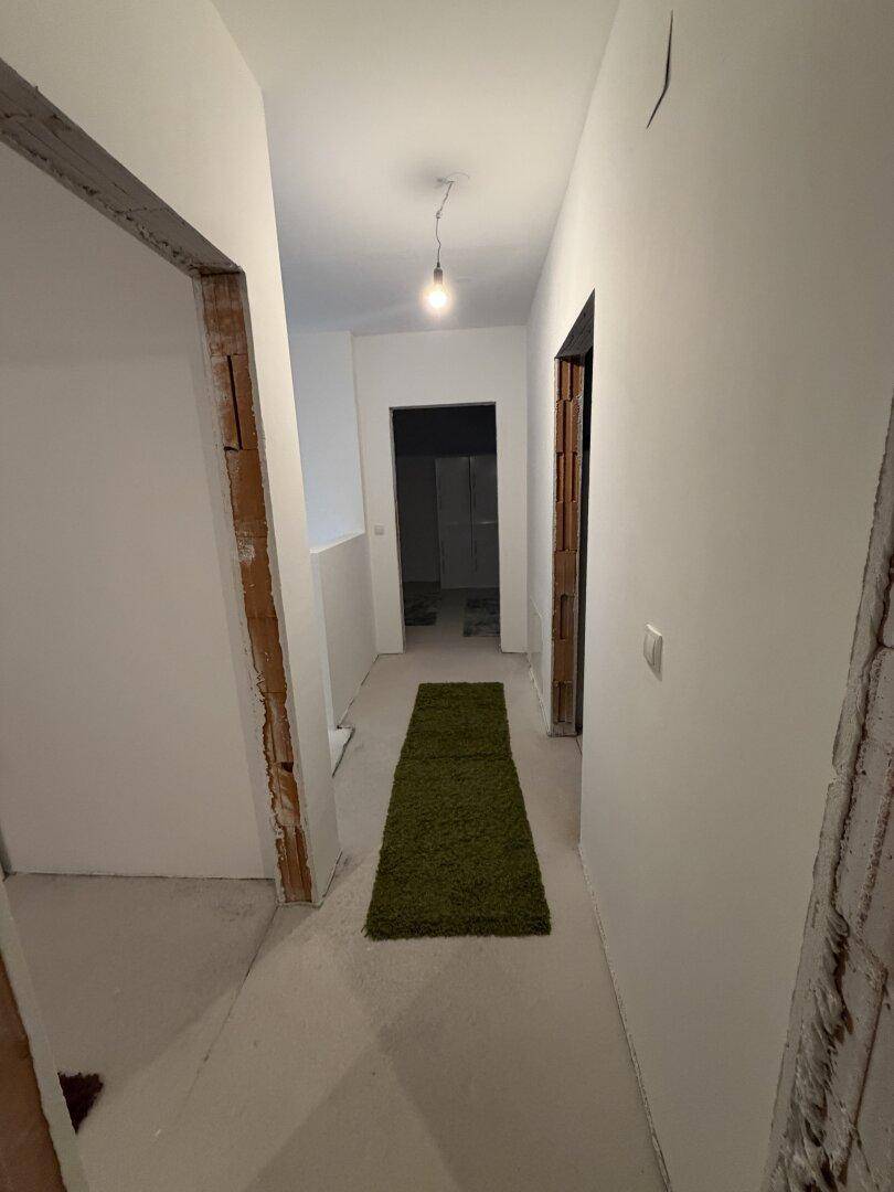 Heller Flur im Rohbau mit grünem Teppichläufer, der zu weiteren Räumen führt, noch unfertig.