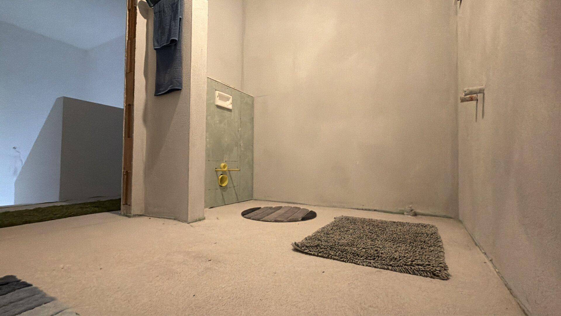 Badezimmer im Rohbau mit vorbereiteter Installation für ein wandhängendes WC und Dusche, modern geplant.