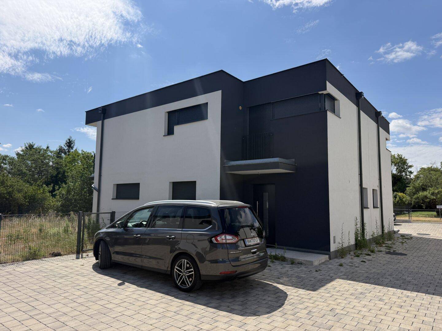 Modernes Doppelhaus mit dunkler und heller Fassade, gepflastertem Vorplatz und Parkmöglichkeit.