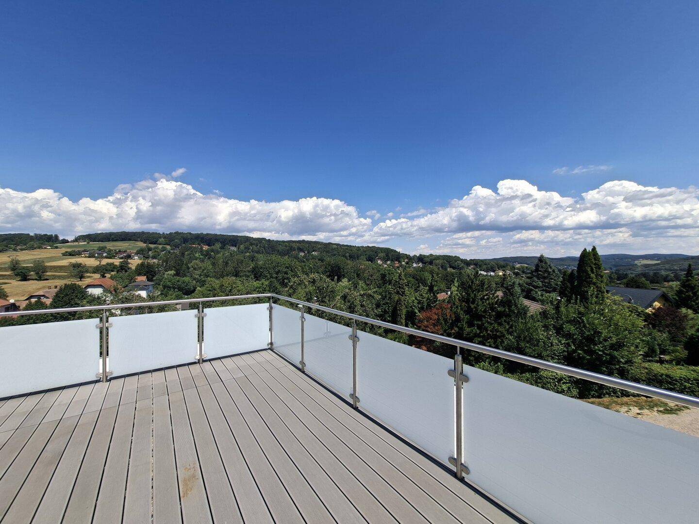 Große Dachterrasse mit modernem Glasgeländer und weitem Blick über die grüne Landschaft.