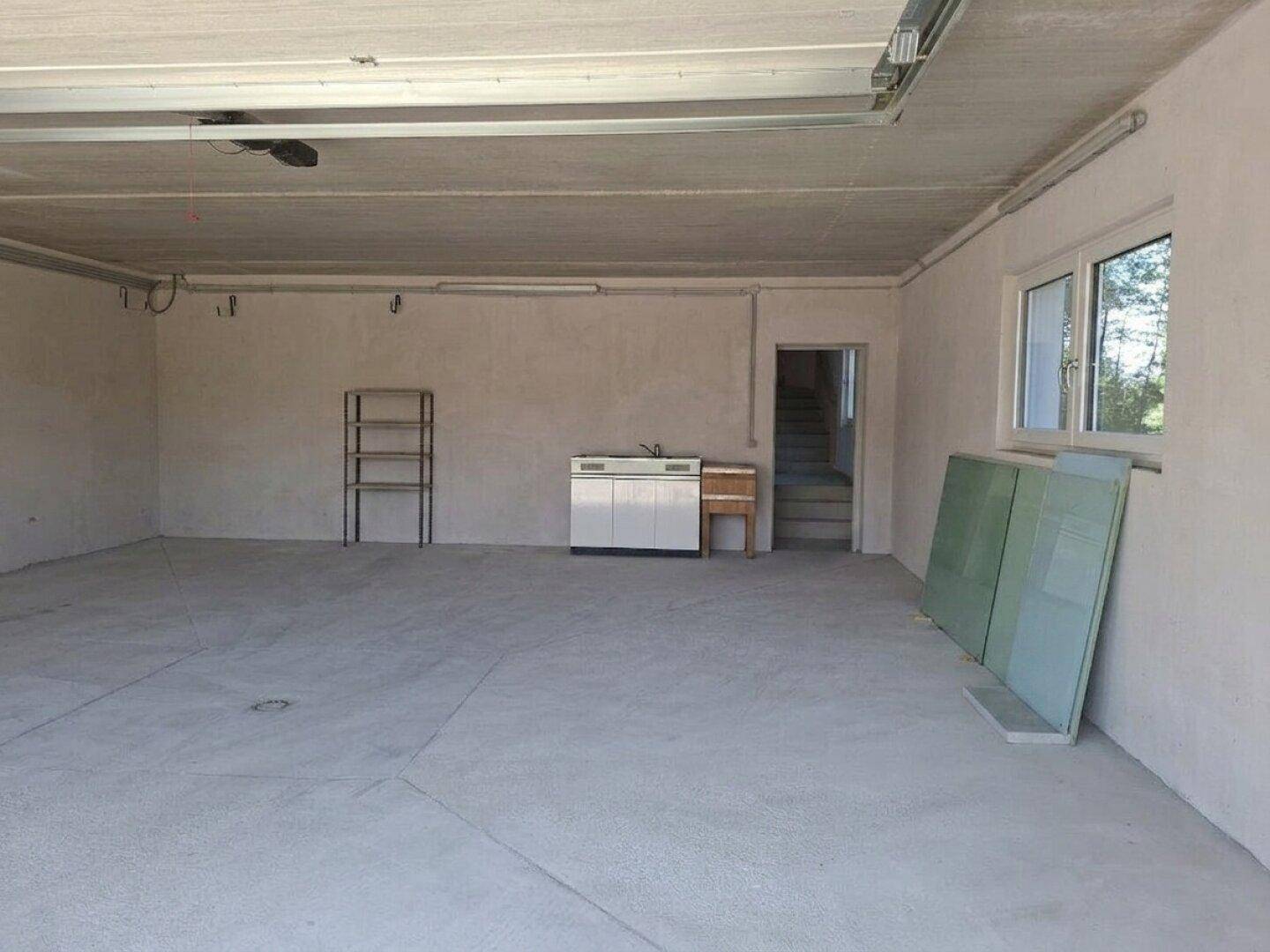 Geräumige Garage mit Betonboden, einem Fenster und einem praktischen Waschbecken.