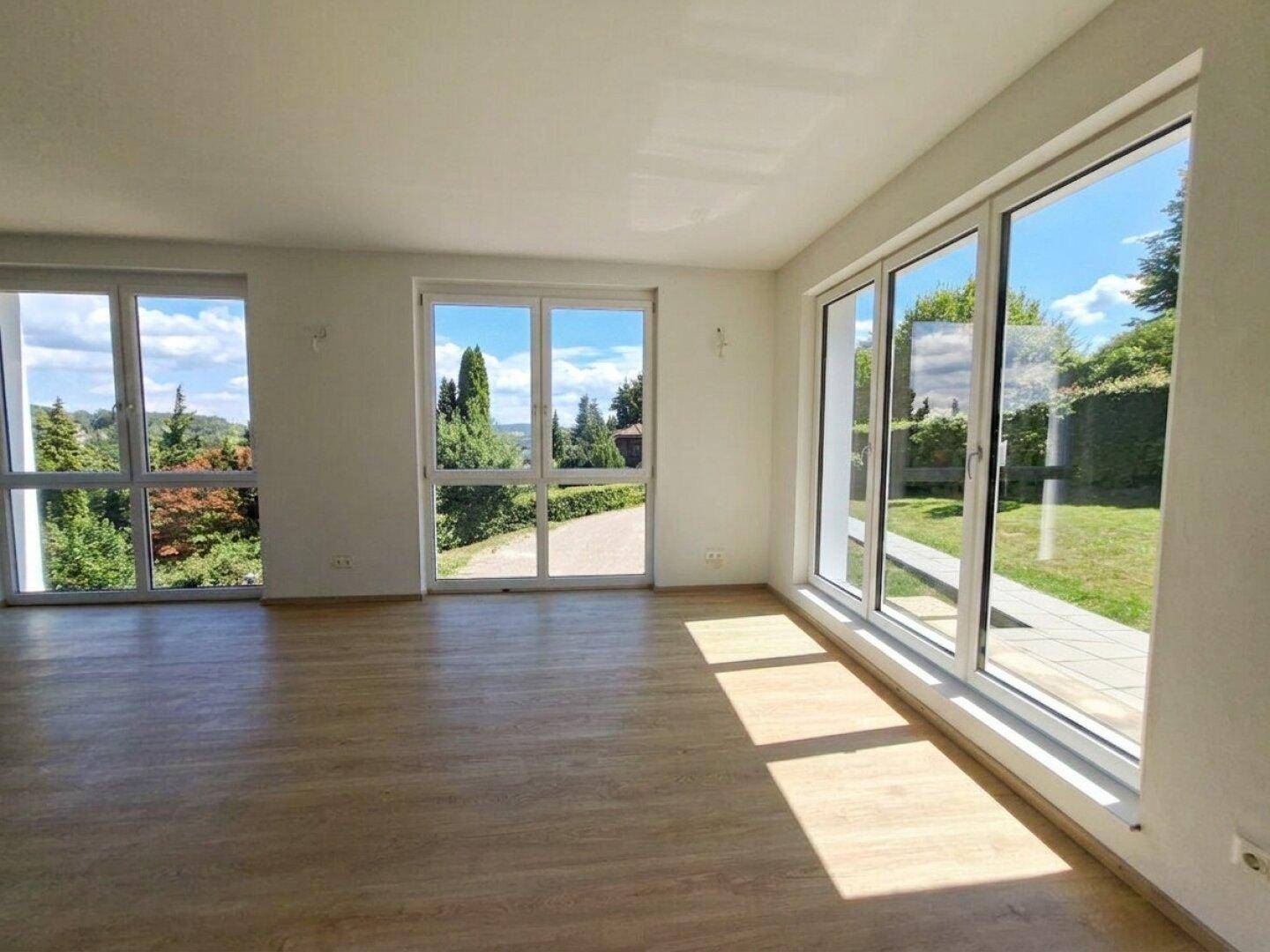 Helles Wohnzimmer mit großen Fenstern, Laminatboden und direktem Zugang zur Terrasse und Garten.
