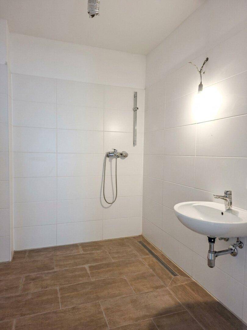 Modernes Badezimmer mit ebenerdiger Dusche, weißen Fliesen und einem einzelnen Waschbecken.