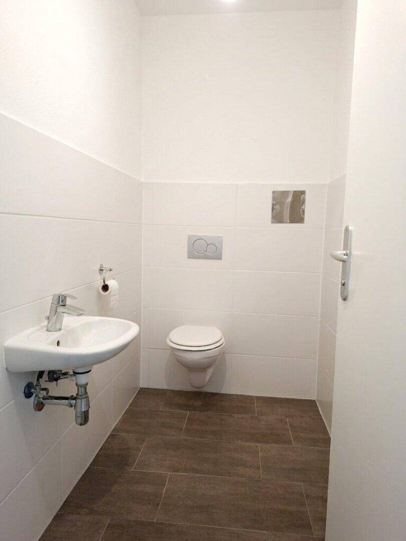 Separates Gäste-WC mit Wand-WC, kleinem Waschbecken und modernen Fliesen in Weiß und Braun.