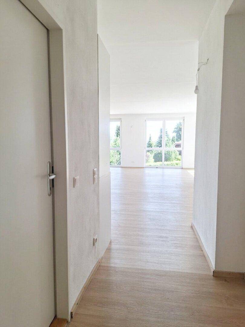 Heller Flur mit Laminatboden, weißen Wänden und Blick in einen offenen Wohnbereich.