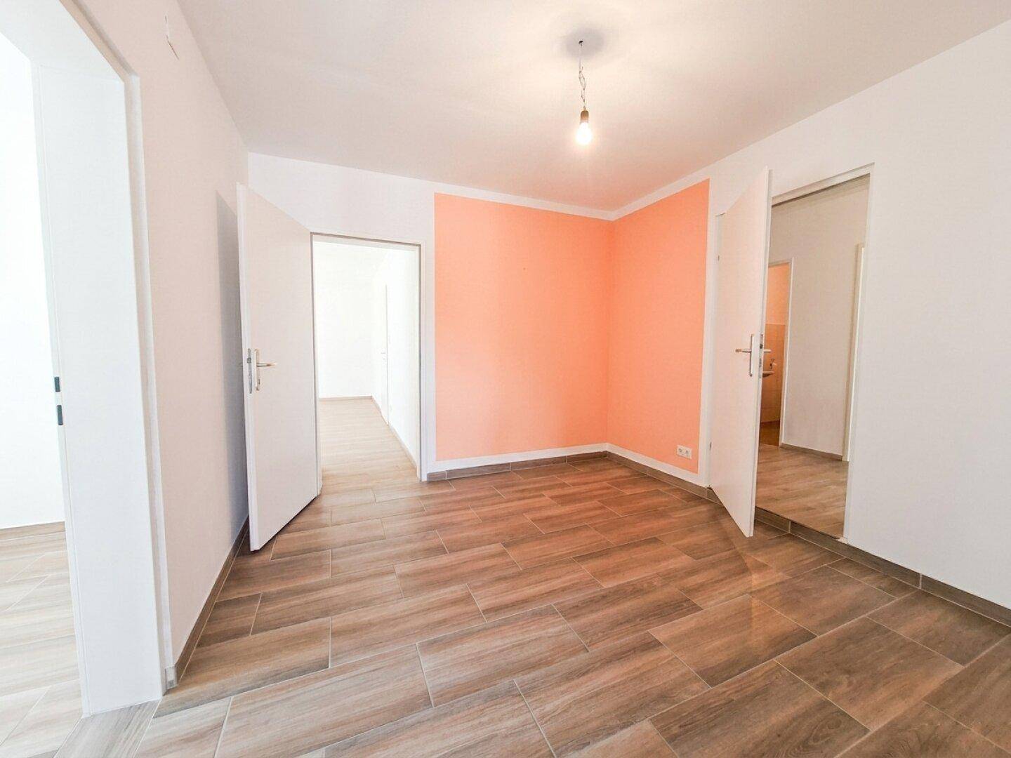 Flur mit Fliesenboden in Holzoptik und einer Akzentwand in warmem Pfirsichton.