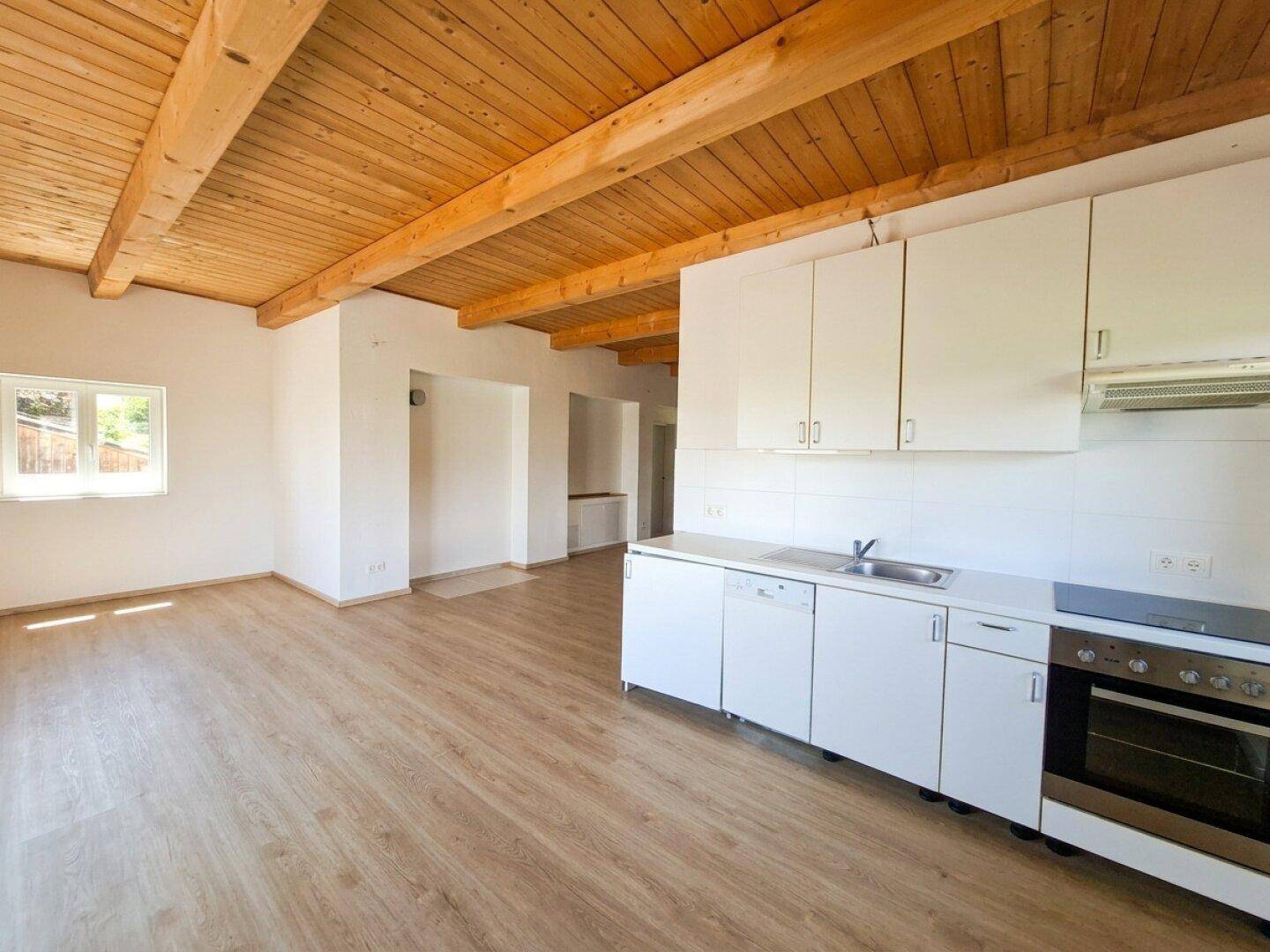 Geräumiger offener Wohnbereich mit Küchenzeile, sichtbaren Holzbalken und Laminatboden.