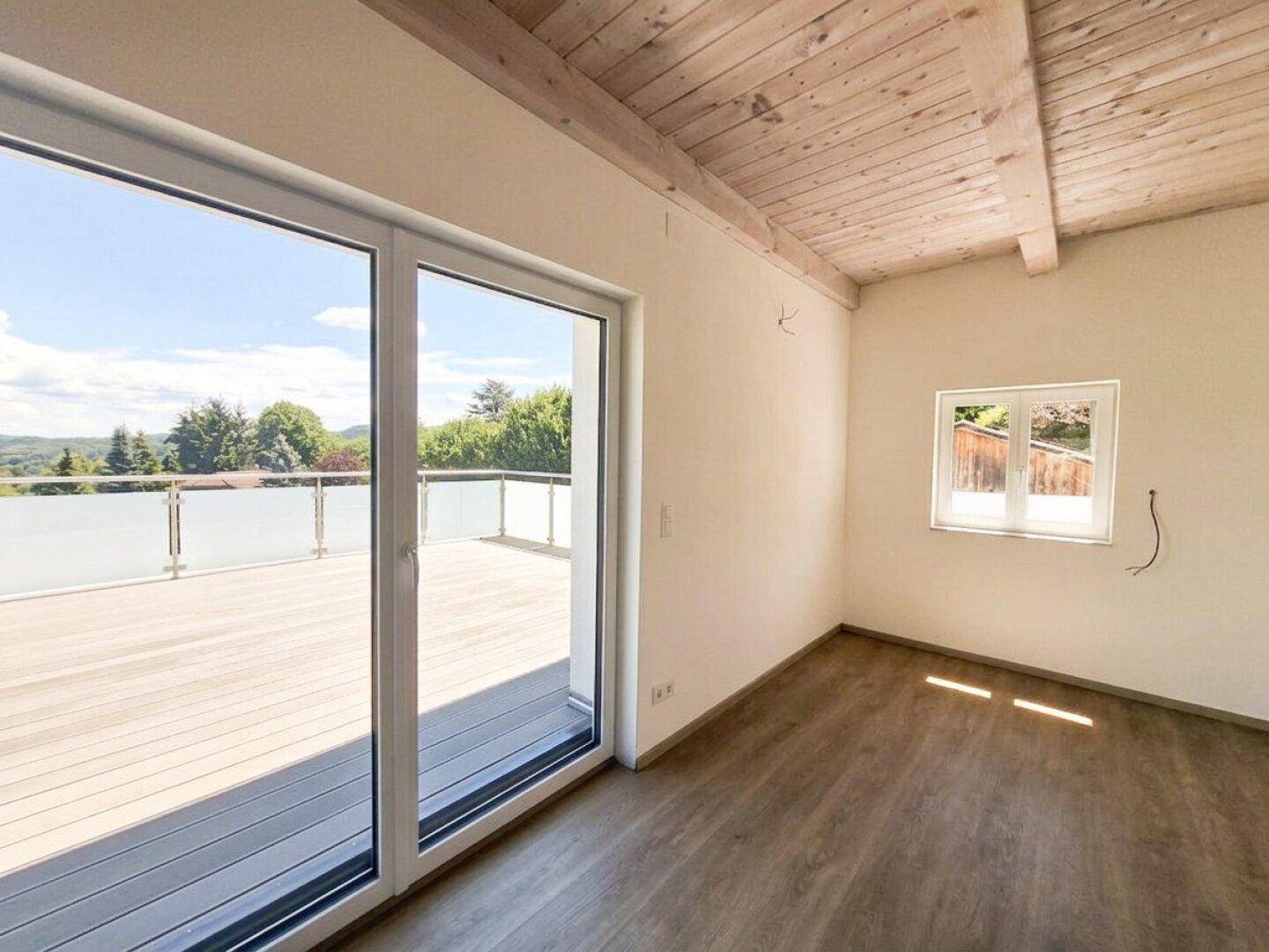 Schlafzimmer mit Holzbalkendecke, Laminatboden und direktem Zugang zu einer großen Dachterrasse.