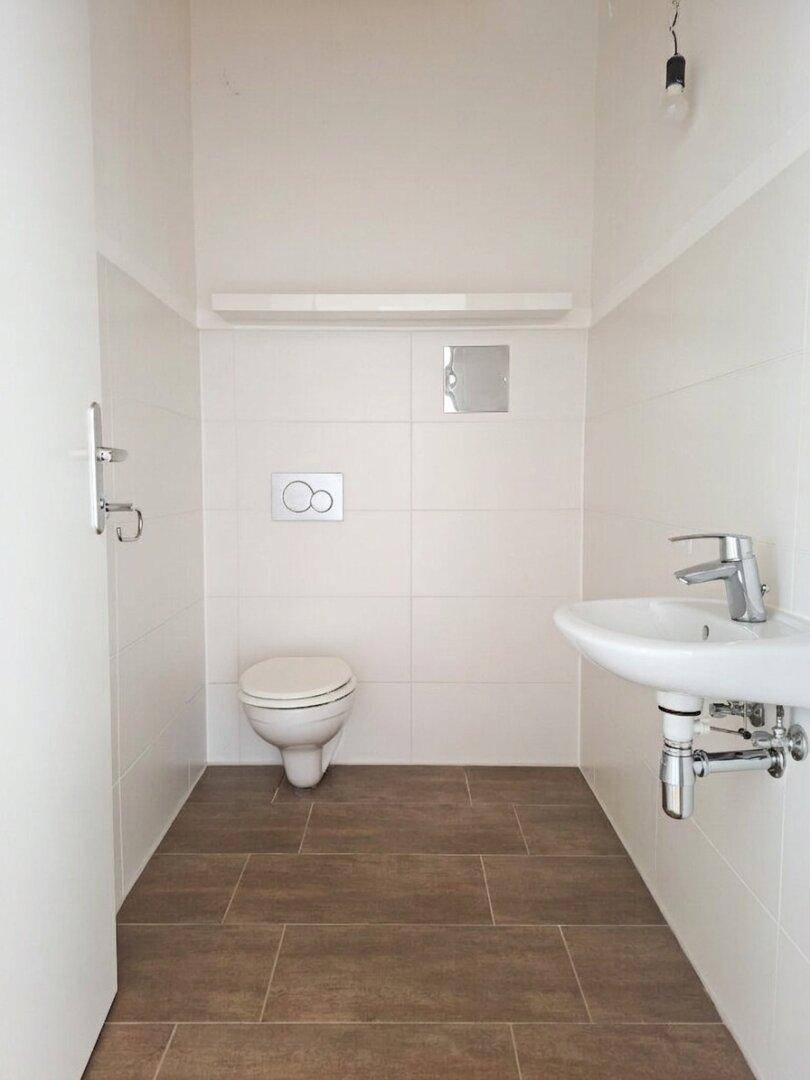 Modernes Gäste-WC mit Wand-WC, kleinem Waschbecken und weißen Fliesen in Kombination mit Braun.