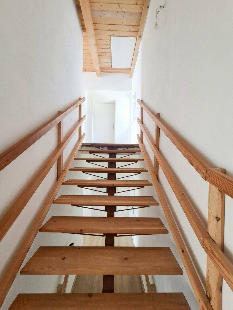 Holztreppe führt in den oberen Bereich des Hauses mit sichtbarer Holzdecke und hellem Anstrich.