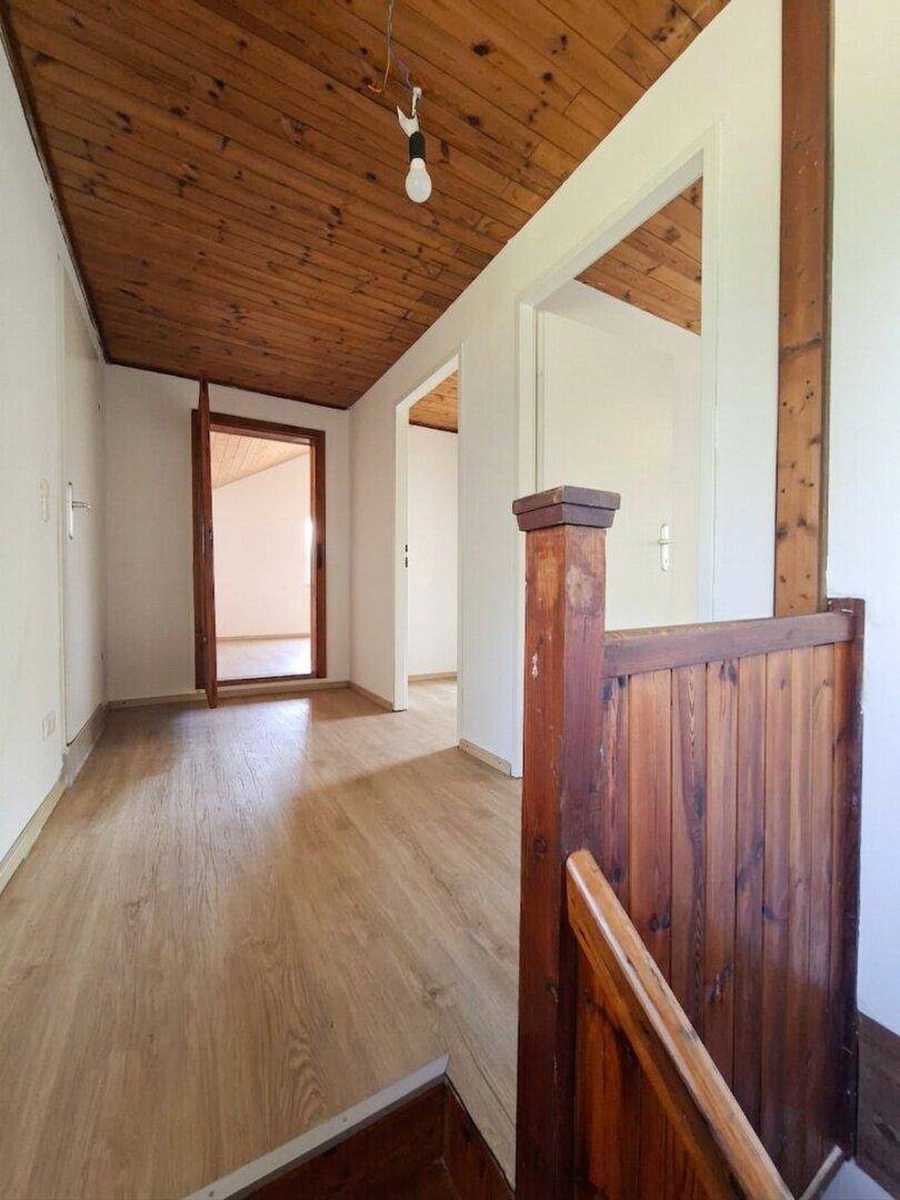 Flur im Obergeschoss mit Holzbalkendecke, Laminatboden und rustikalem Holzgeländer.