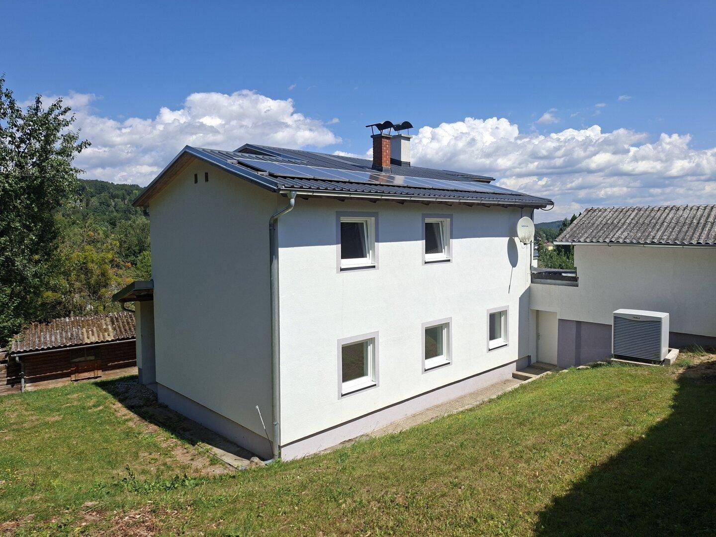 Seitenansicht des Hauses mit Photovoltaikanlage auf dem Dach und einer Wärmepumpe im Garten.