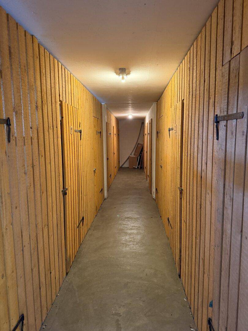 Langer Kellergang mit zahlreichen Holzverschlägen für zusätzlichen Stauraum.