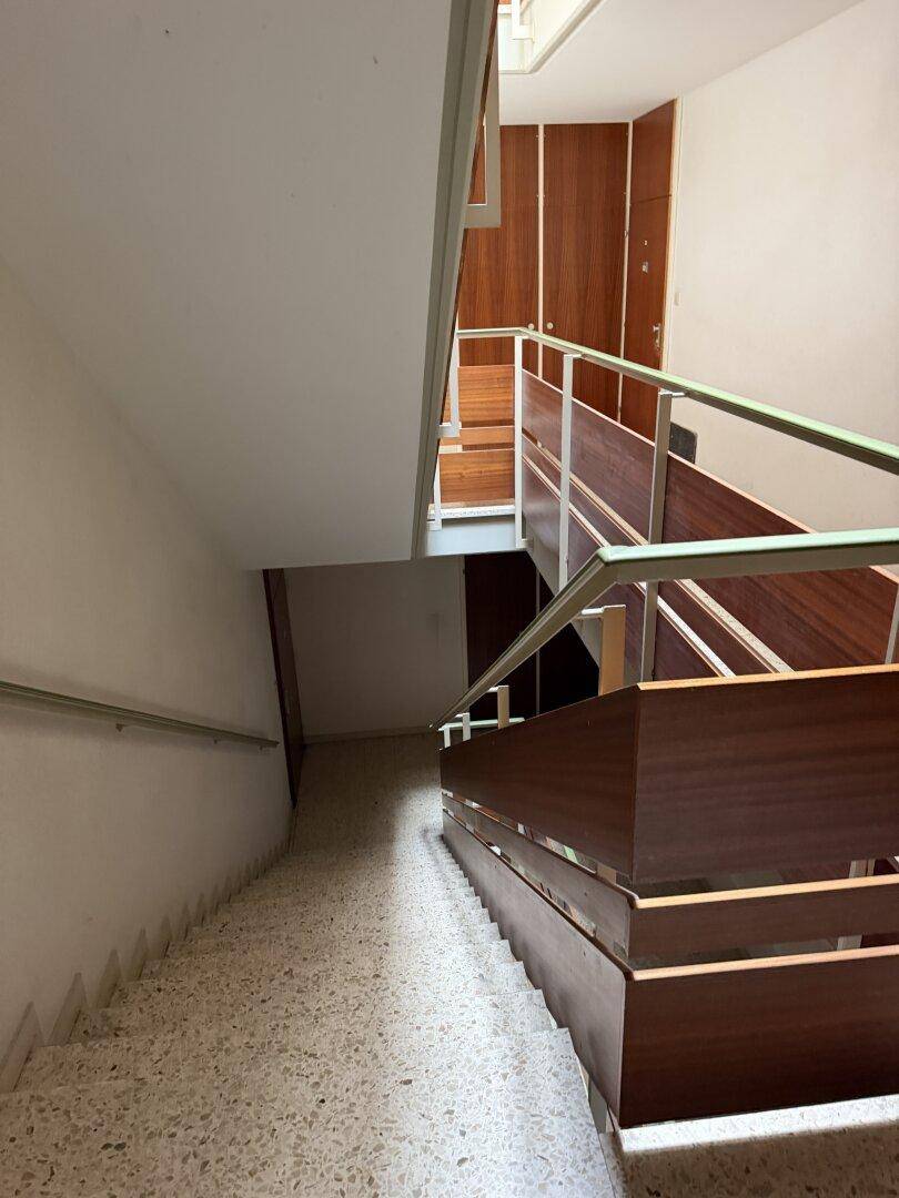 Treppenhaus mit Terrazzoboden und Holzgeländer, das die verschiedenen Etagen verbindet.