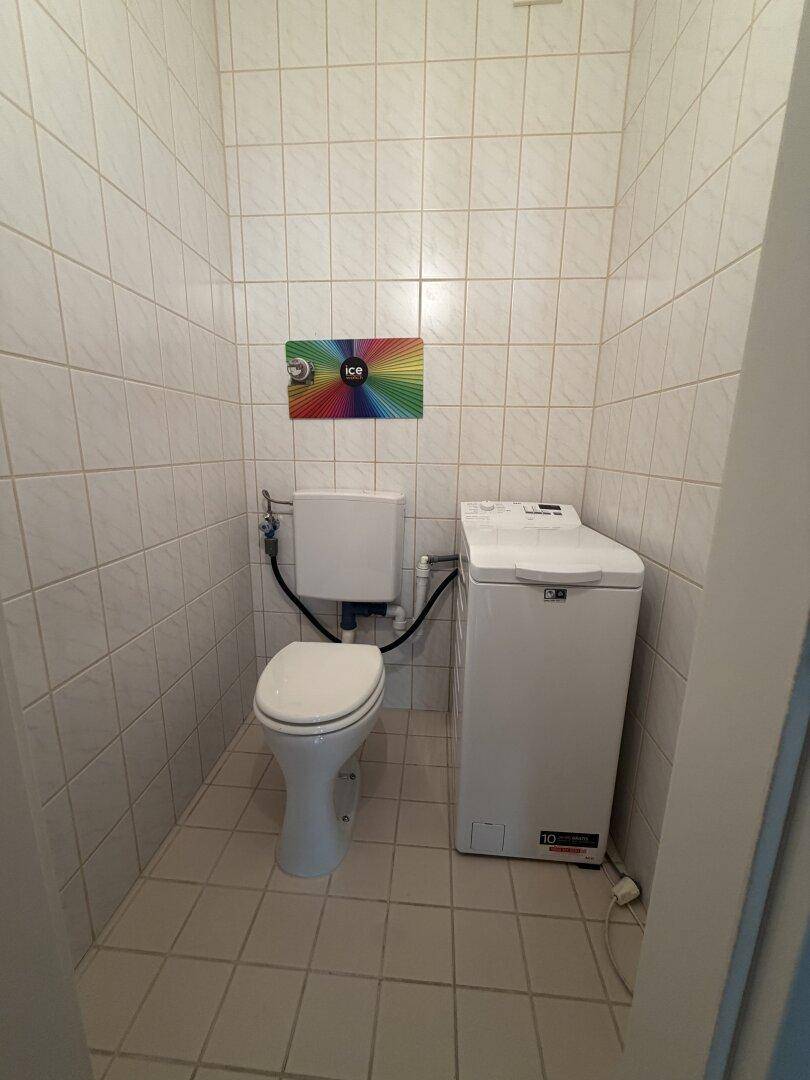 Separates WC mit Toilette und Waschmaschine, komplett gefliest in hellen Farben.