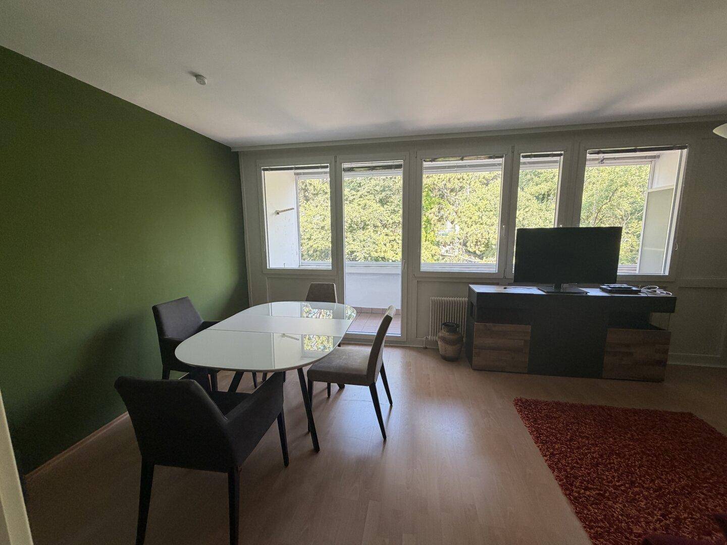 Heller Essbereich mit modernem Tisch und Stühlen, umgeben von großen Fenstern mit Blick ins Grüne.