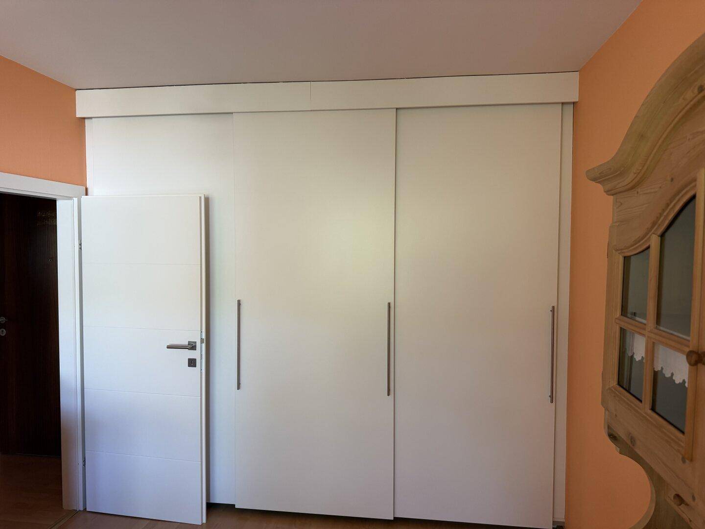 Großer, weißer Einbauschrank mit Schiebetüren in einem Zimmer mit orangefarbenen Wänden.