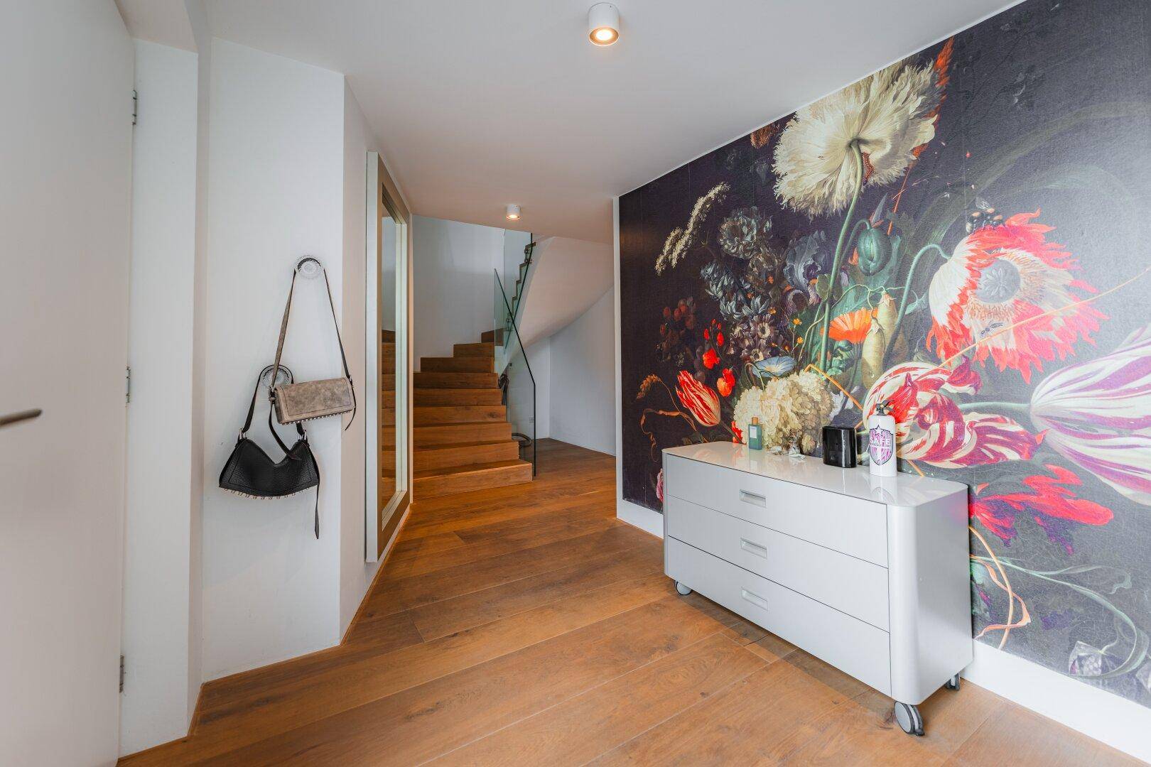 Einladender Flur mit Holzboden, auffälliger Blumentapete und eleganter Holztreppe.