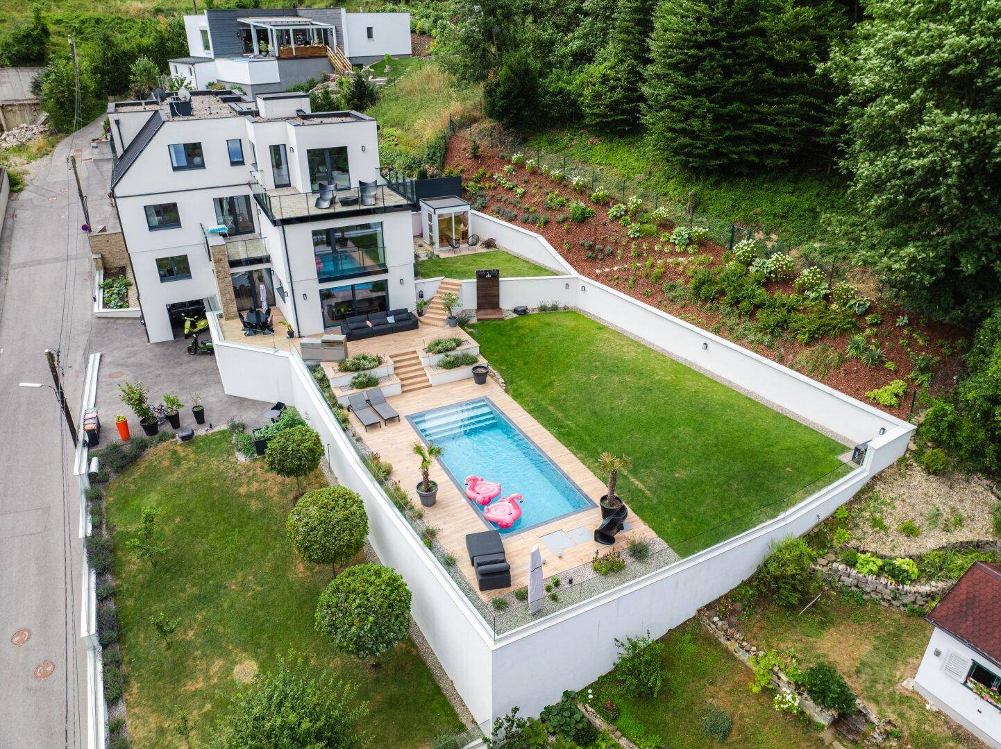 Gesamtansicht der modernen Villa mit Pool, Garten und der umliegenden grünen Landschaft aus der Vogelperspektive.