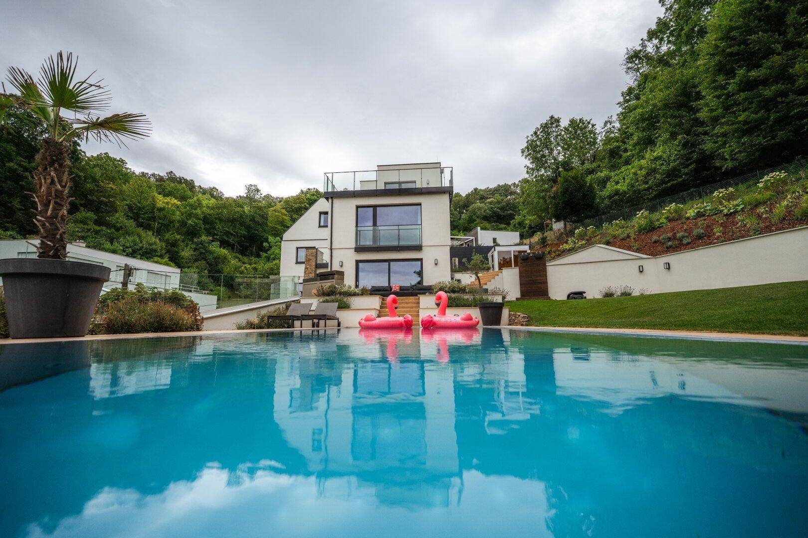 Der blaue Pool spiegelt die moderne Architektur der Villa wider, umgeben von üppigem Grün.