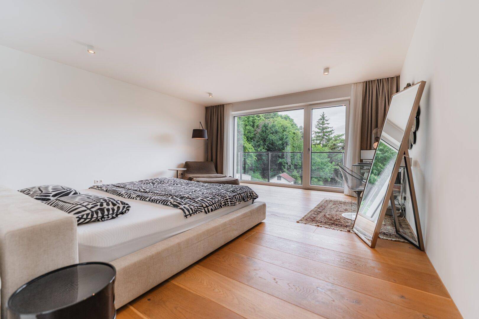Geräumiges Schlafzimmer mit Holzboden, großem Bett und bodentiefen Fenstern mit Blick ins Grüne.