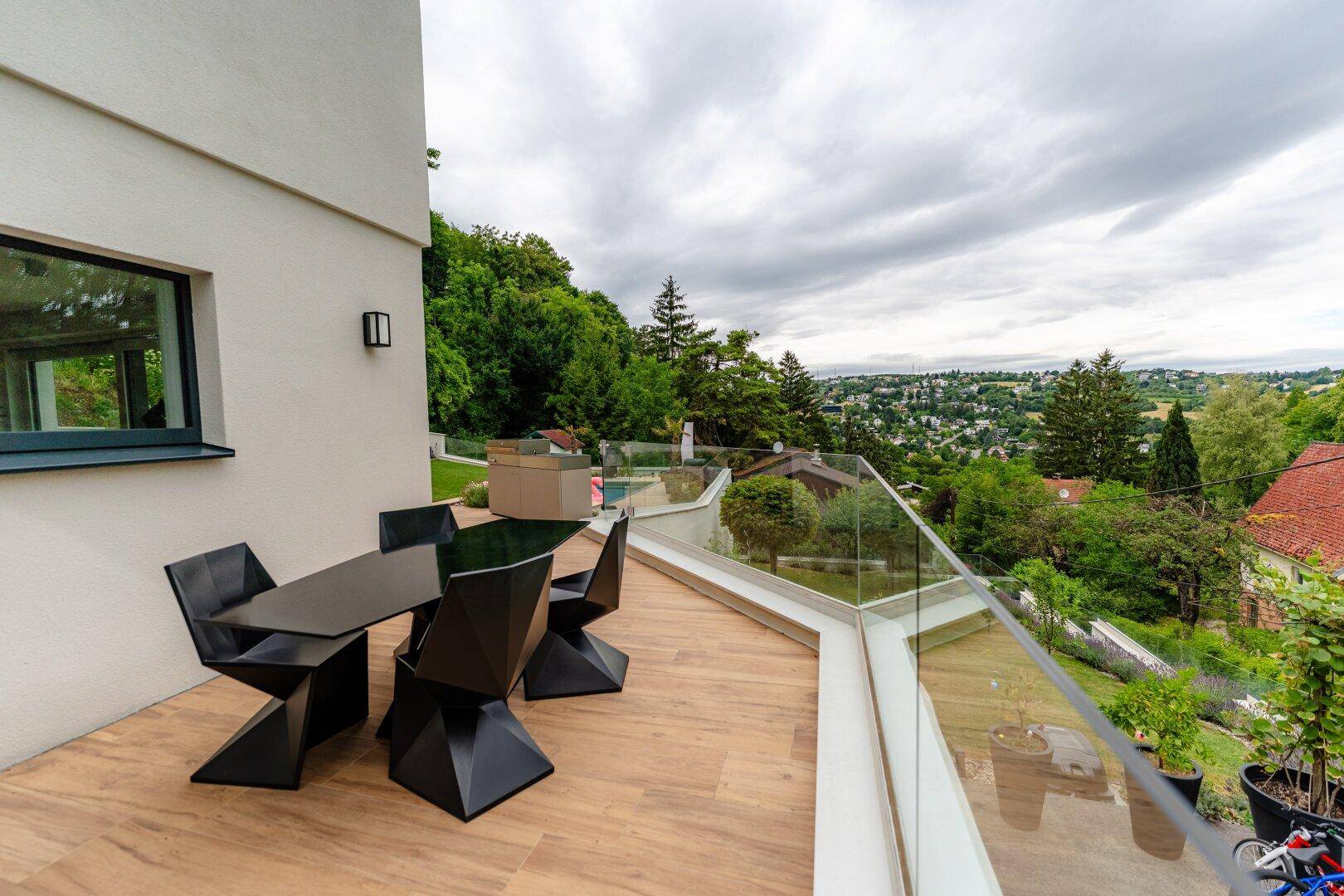 Elegante Terrasse mit modernen Möbeln, Holzbelag und einem weiten Panoramablick ins Grüne.