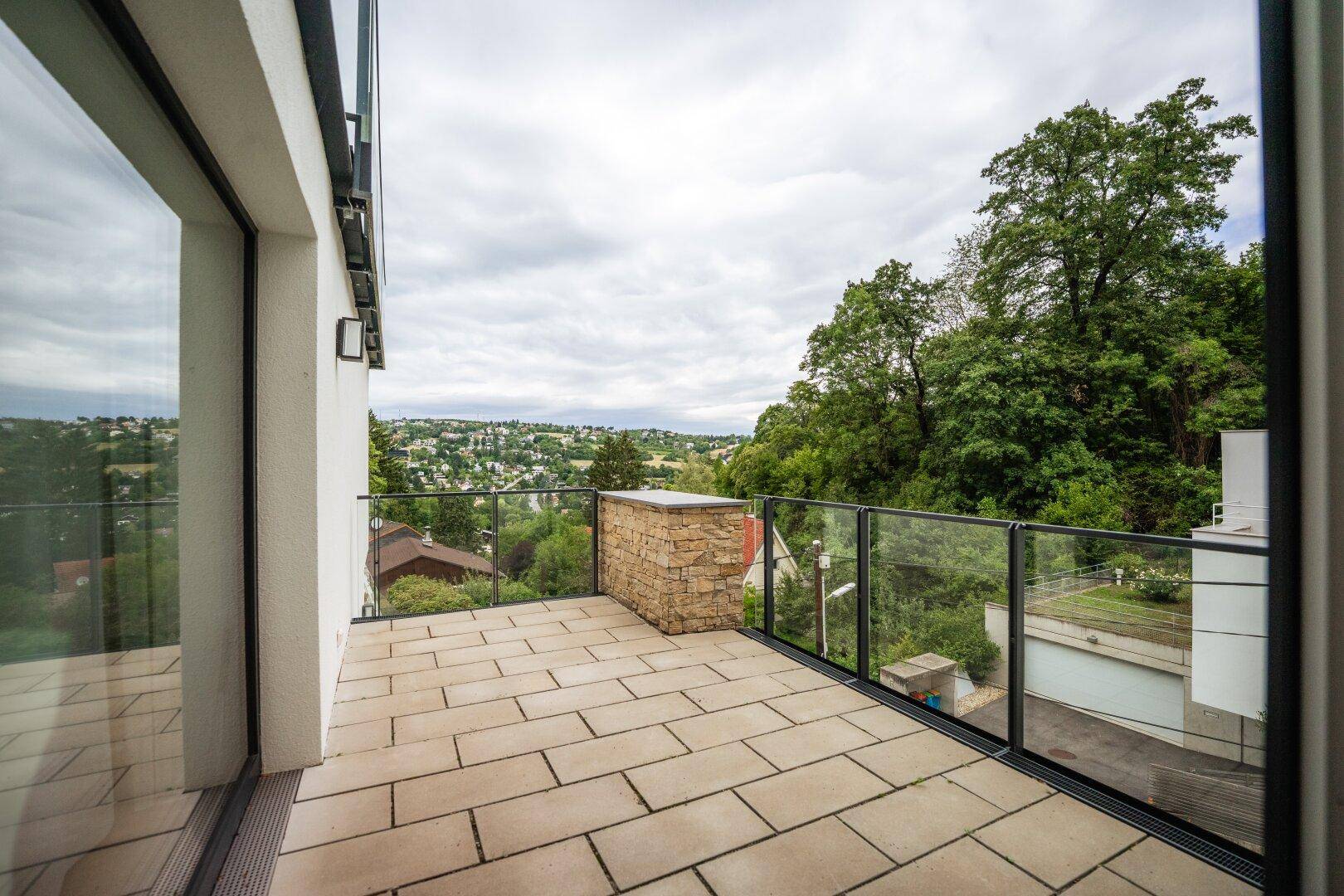 Heller Balkon mit Fliesenboden, Glasgeländer und weitem Ausblick über die Landschaft.