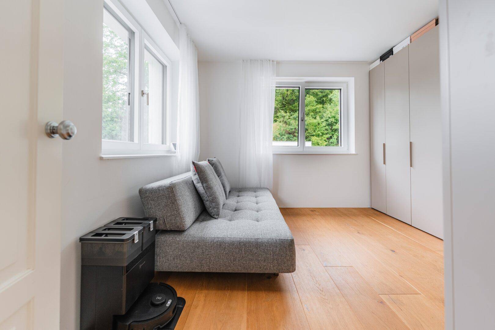 Helles Zimmer mit Holzboden, Schlafsofa und praktischen Einbauschränken.