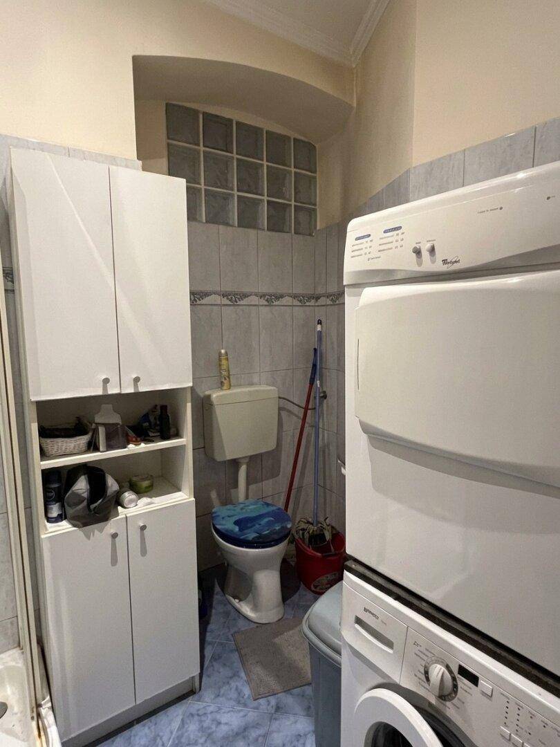 Badezimmer mit Toilette, Waschmaschine und Trockner, ergänzt durch ein Glasbausteinfenster.