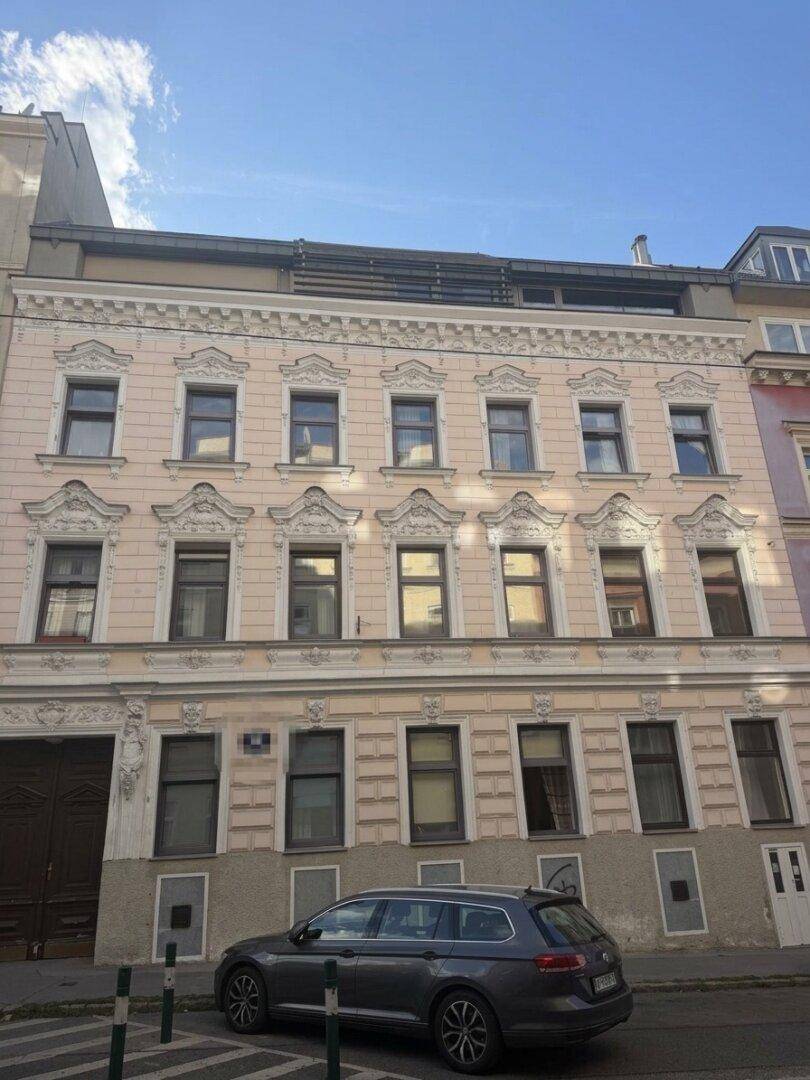 Historische Fassade eines Altbaus mit vielen Fenstern und dekorativen Elementen an einem sonnigen Tag.