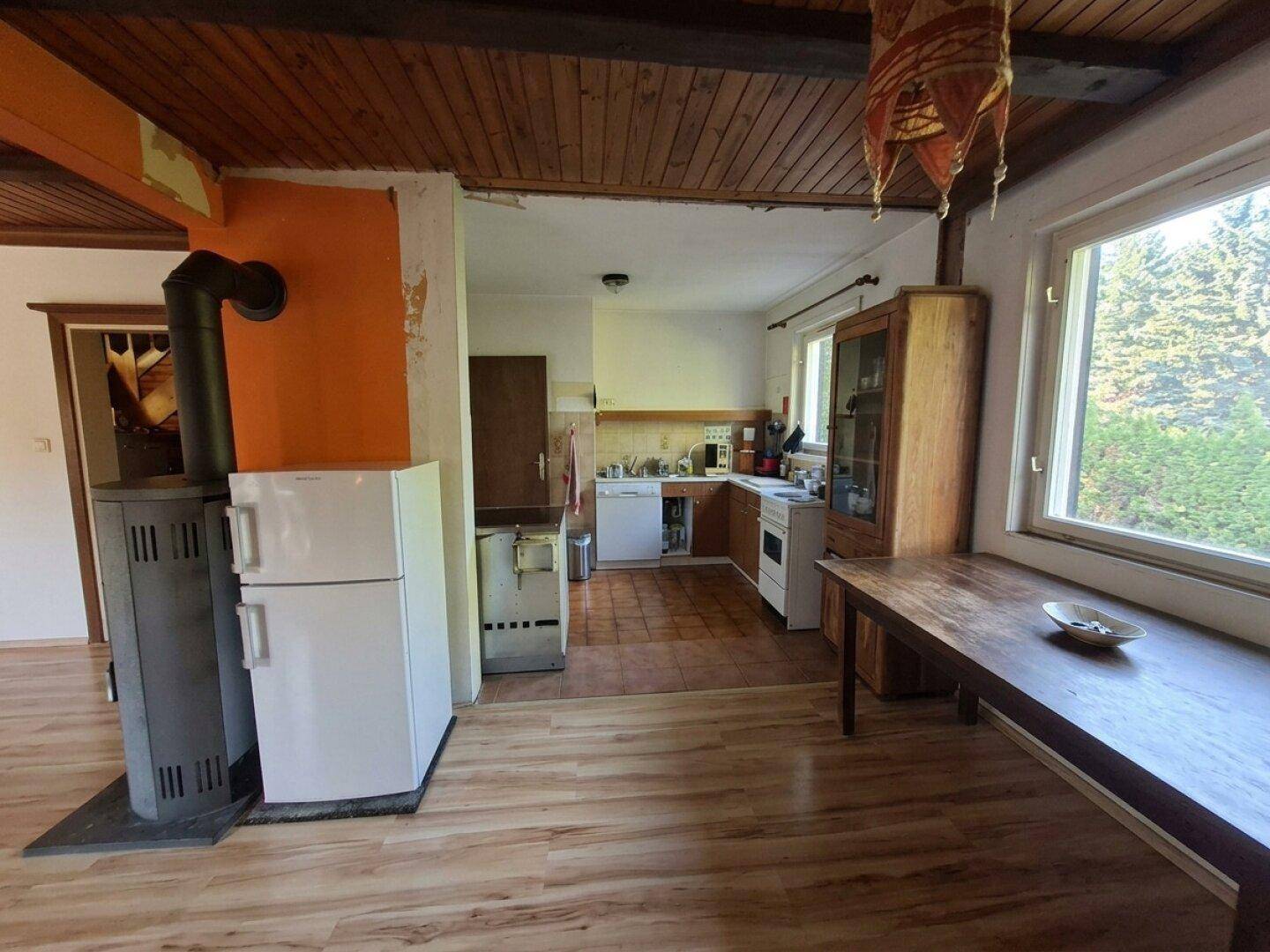 Rustikale offene Küche mit Holzdecke, Kaminofen und Blick ins Grüne.